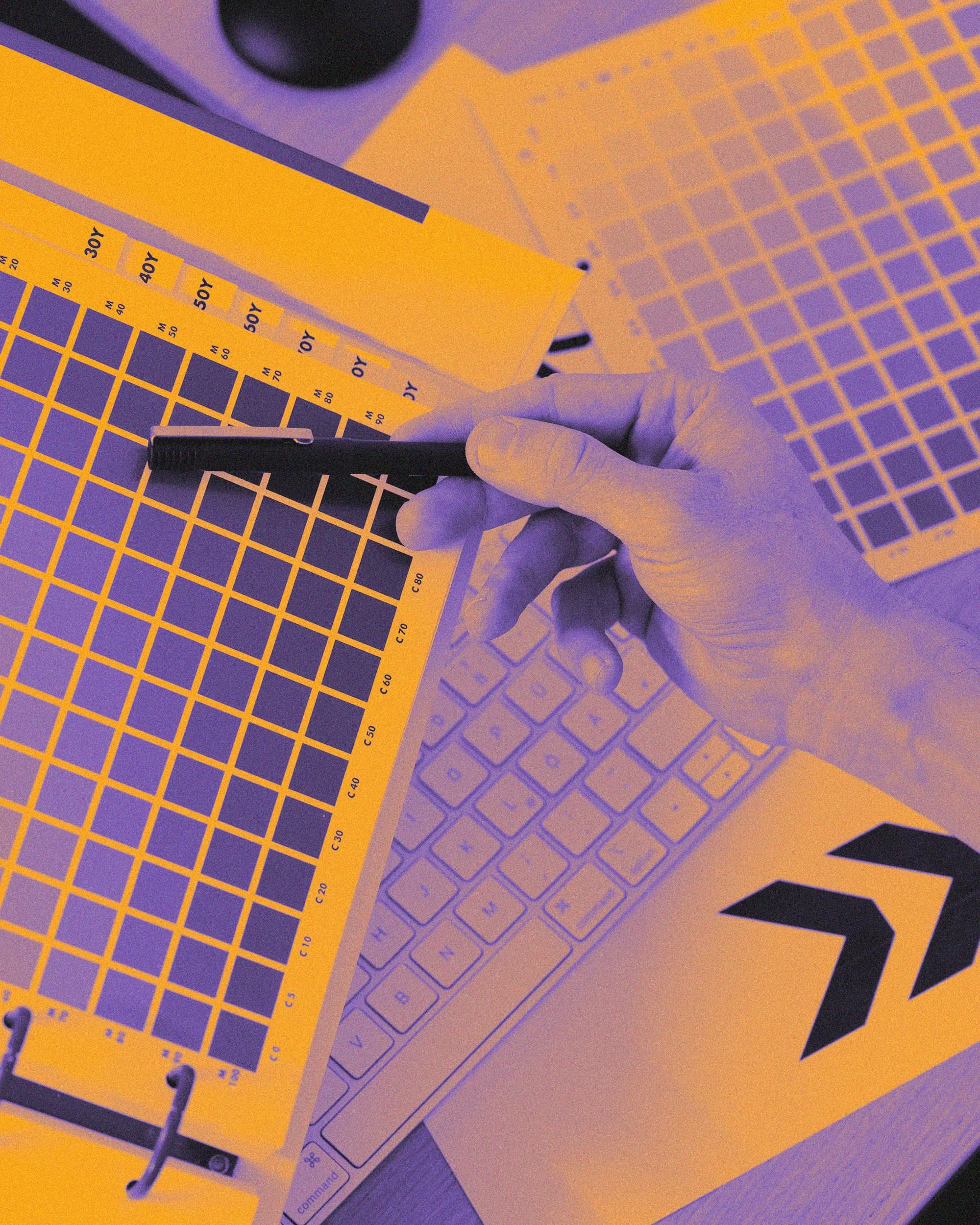 Hands drawing a grid layout next to a keyboard, tinted in violet and orange