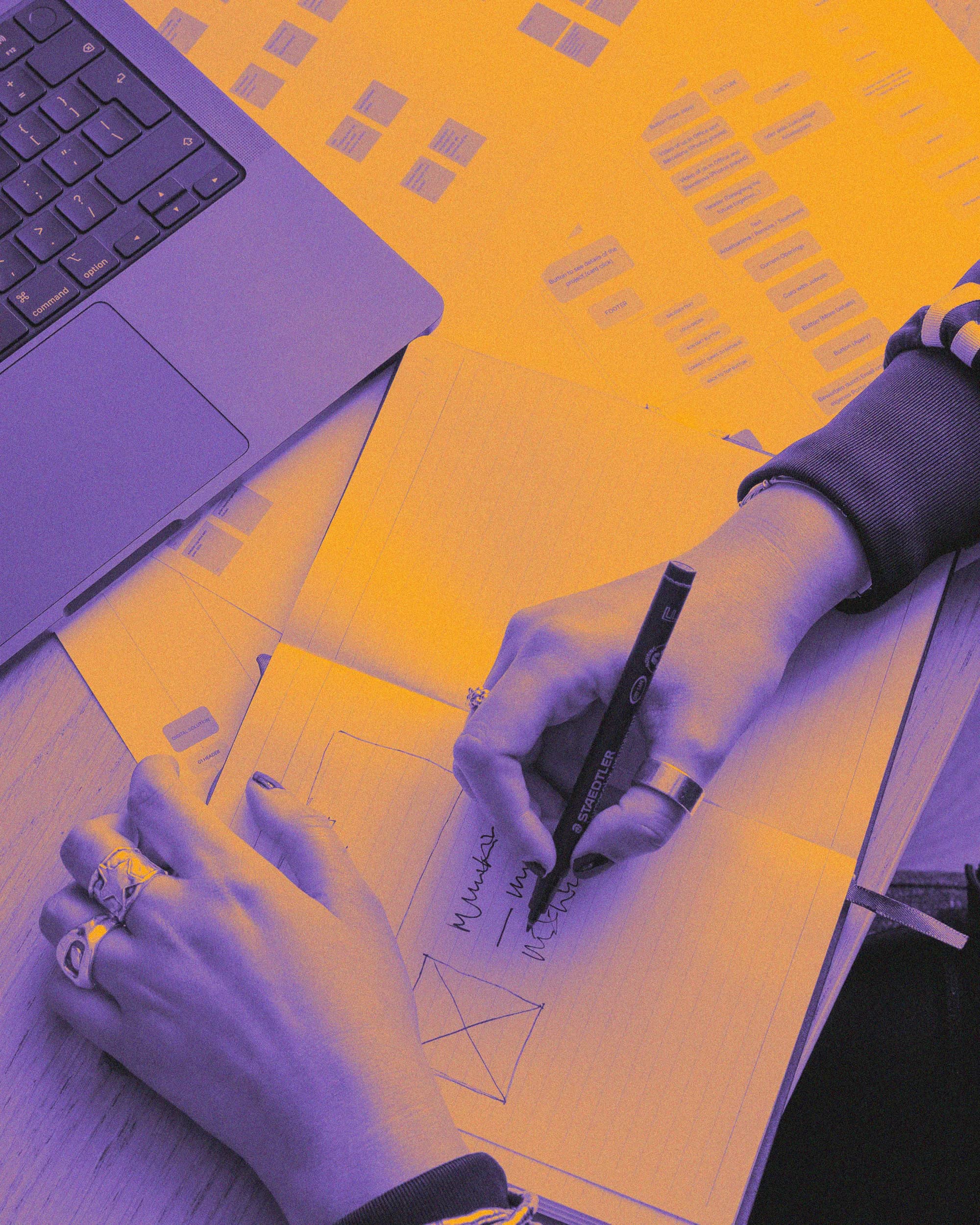 Hand sketching a concept on paper next to a laptop, tinted in violet and orange